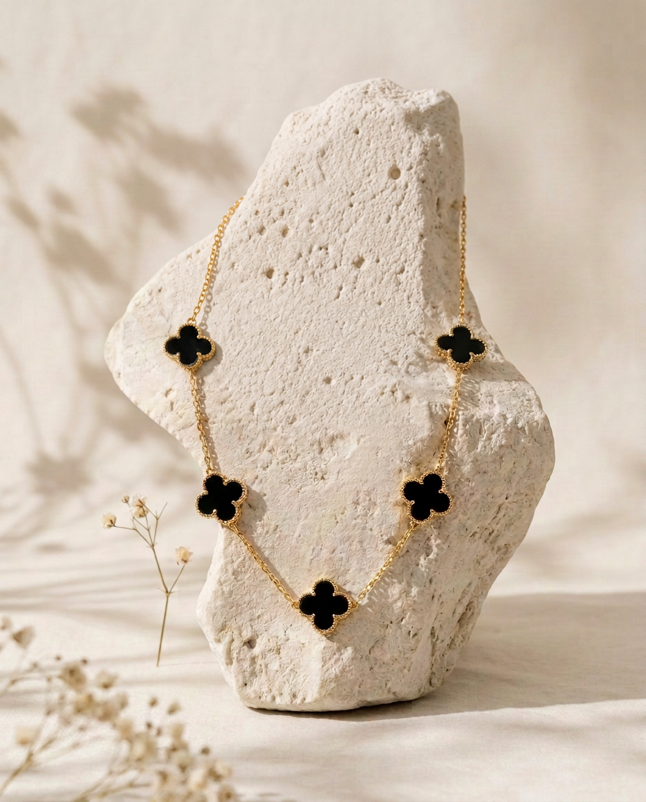 Collier doré à cinq trèfles noirs sur un support en pierre claire